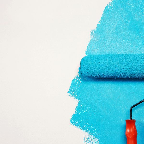 Paint roller applying bright blue paint on a white wall.