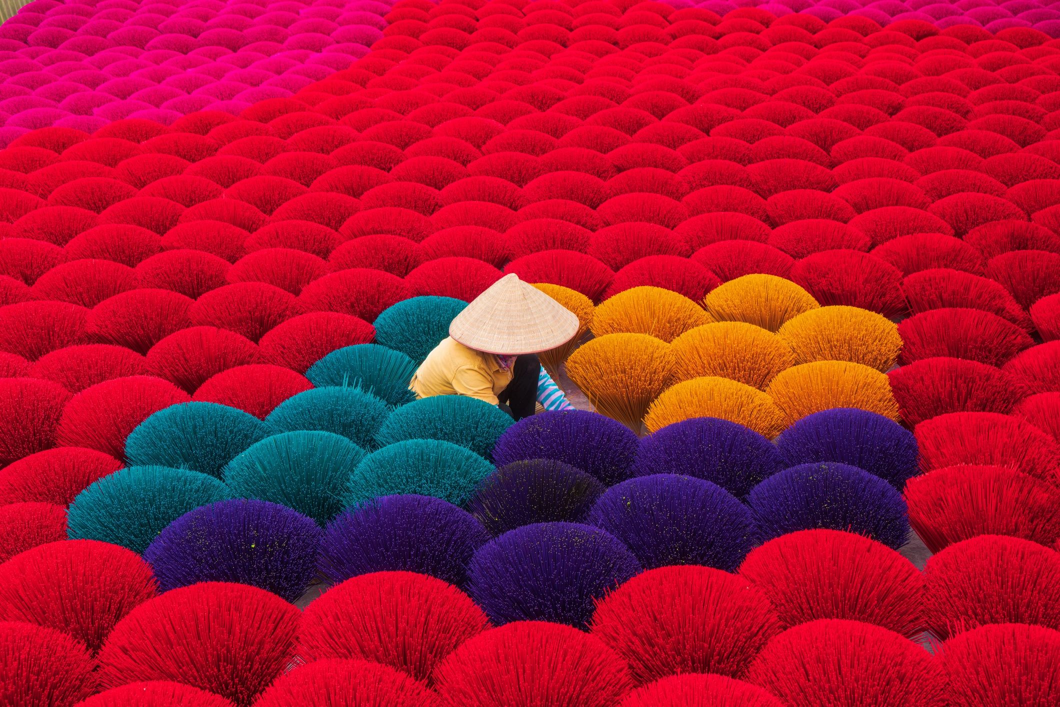 Colorful bundles of incense sticks with a person in a traditional hat.