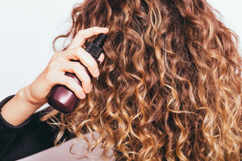 Close-up young woman applying cosmetic oil on her thick naturally curly hair