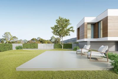 Modern backyard with deck, two cushioned chairs, and a tree against a clear sky.