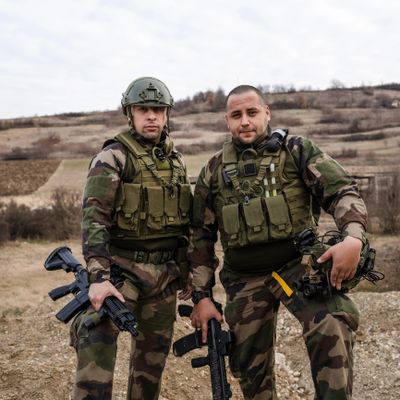 Two soldiers in camouflage gear posing outdoors with rifles.