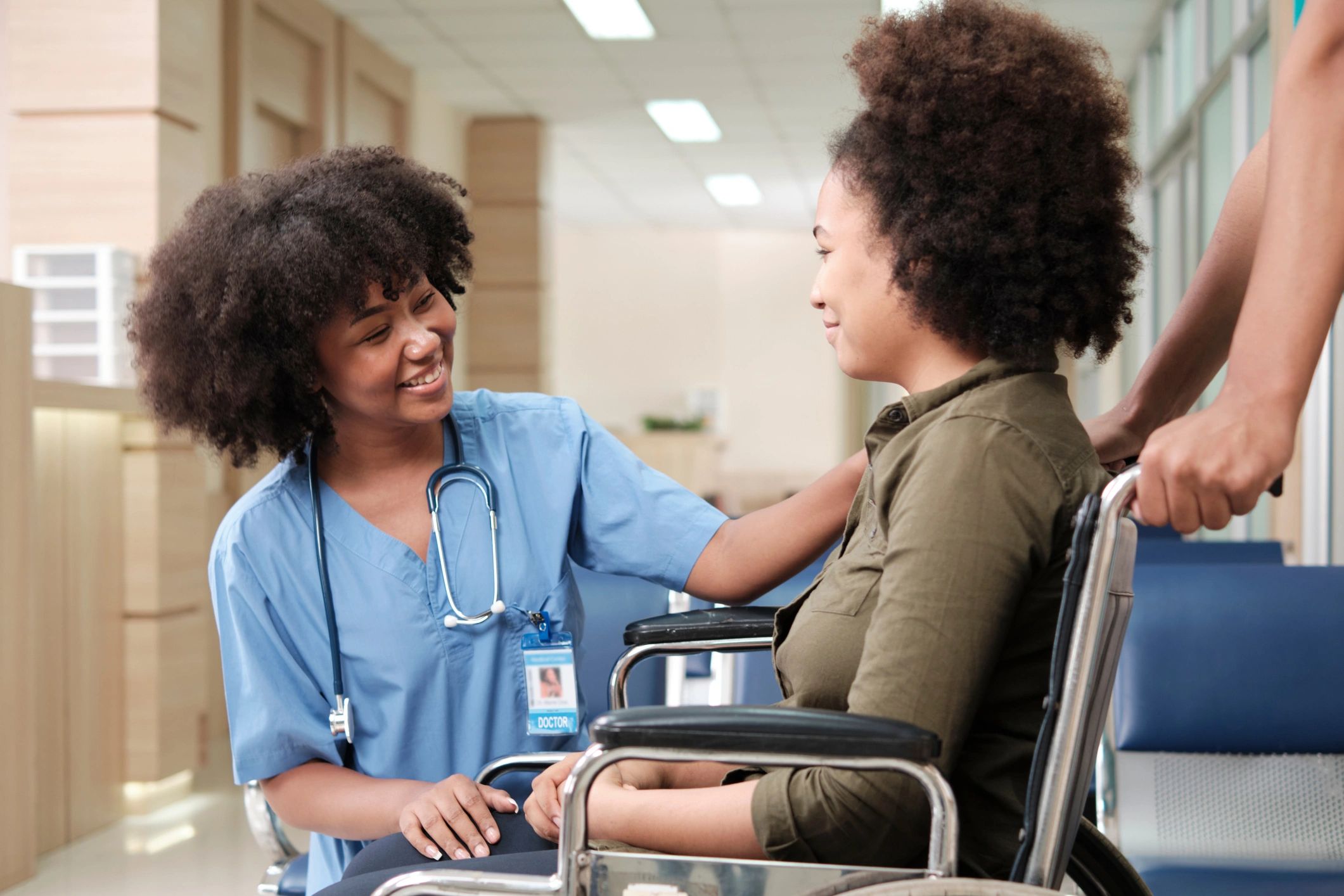 Nurse bent down smiling at a teen girl in a wheelchair.