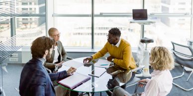 Four colleagues engaged in a meeting around a glass table in a bright office.