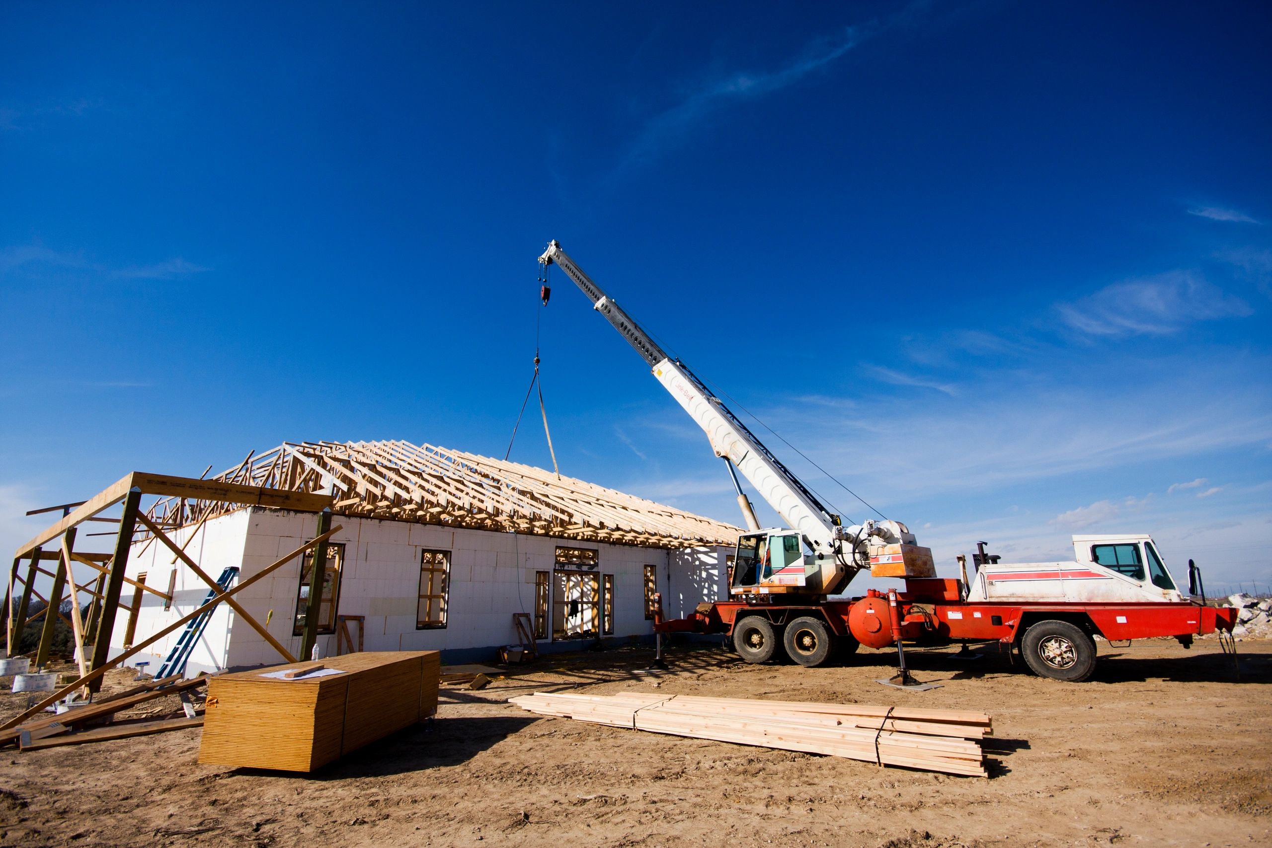 Crane assembling wooden roof trusses on a building under clear blue sky.