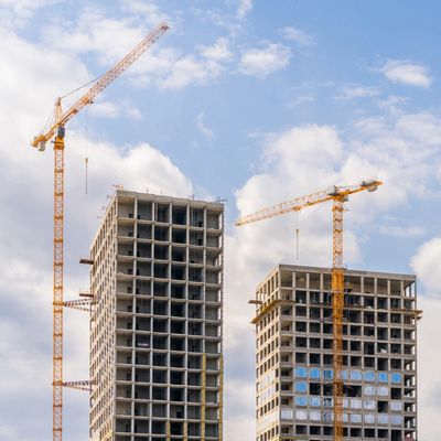 Two construction cranes working on high-rise buildings under a partly cloudy sky.