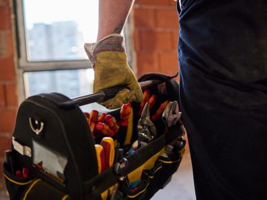 A worker holding a tool bag filled with various hand tools indoors.