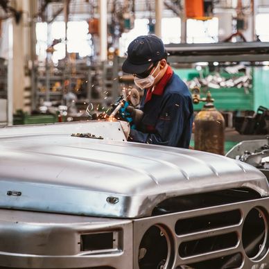 Worker welding metal on a vehicle in a workshop.