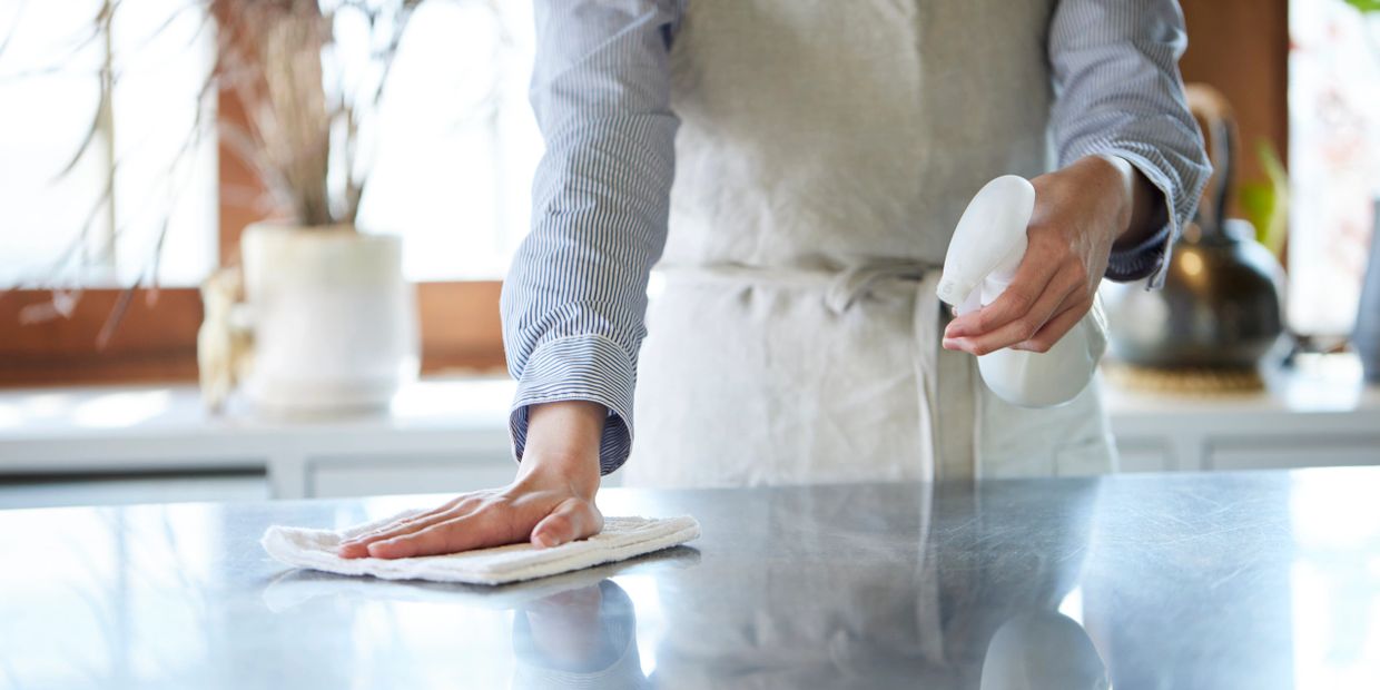 Person cleaning a countertop with spray bottle and cloth.