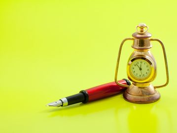 A vintage lantern clock and a red fountain pen on a bright yellow surface.