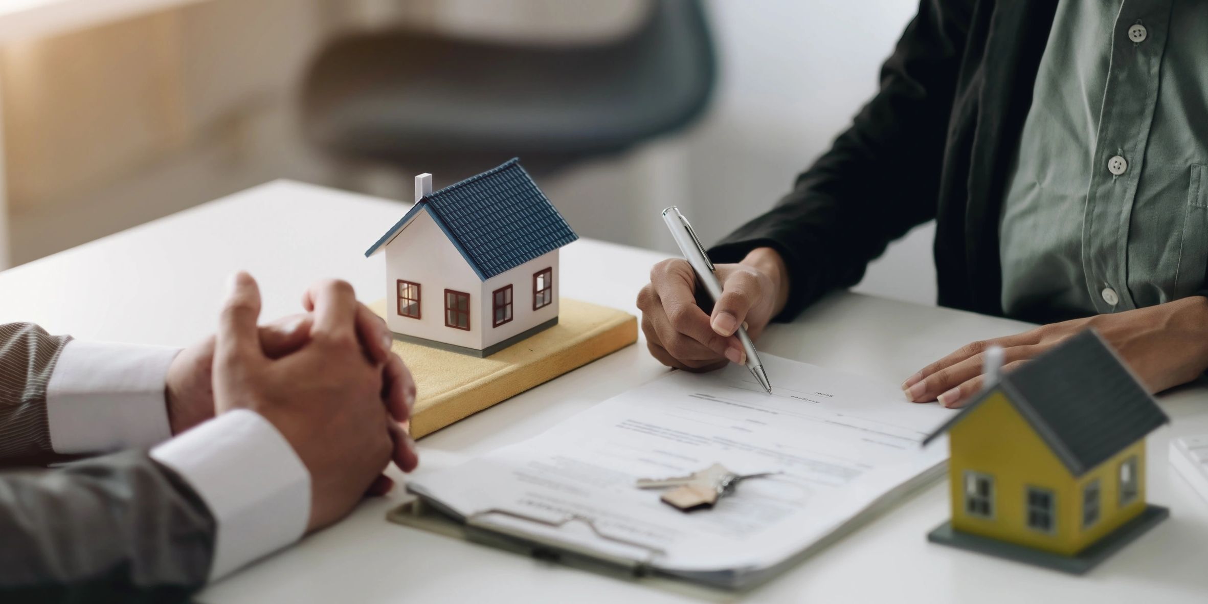 Two people reviewing loan paperwork model houses and keys on the table mortgage approval process