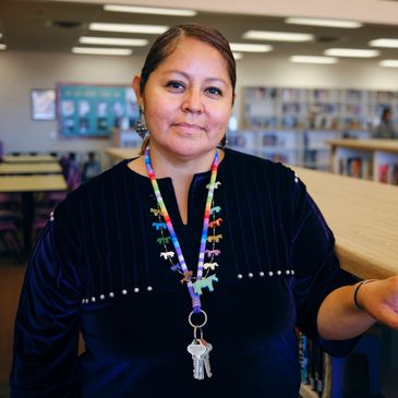 A woman wearing a necklace with colorful animal charms stands in a library.