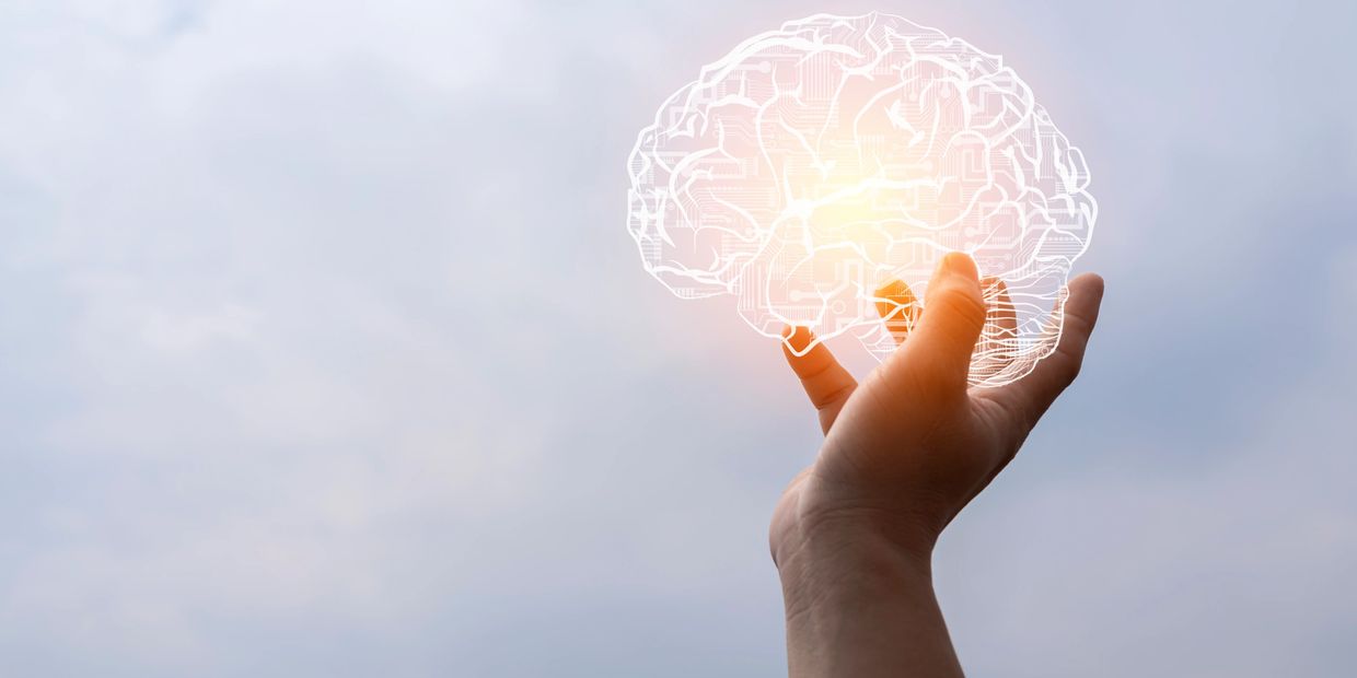 Hand holding a glowing digital brain against a cloudy sky.