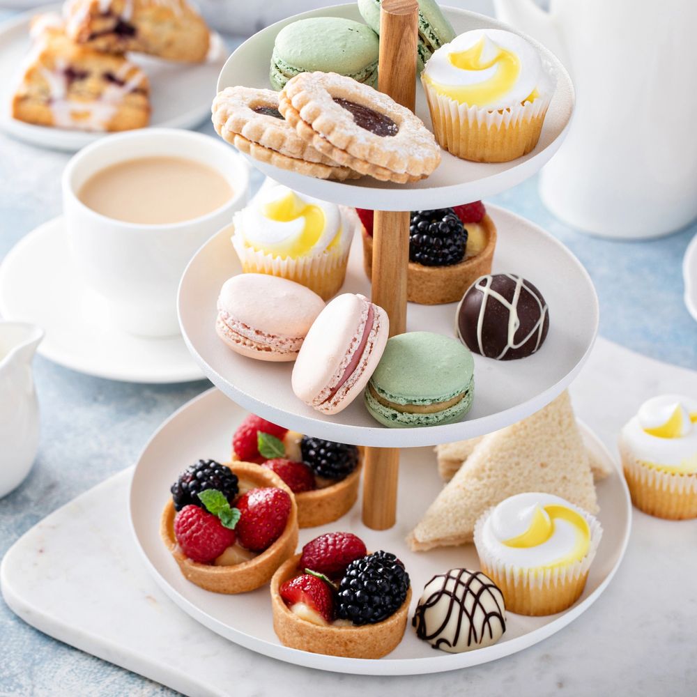 Three-tiered tray with assorted pastries, macarons, tarts, and tea.