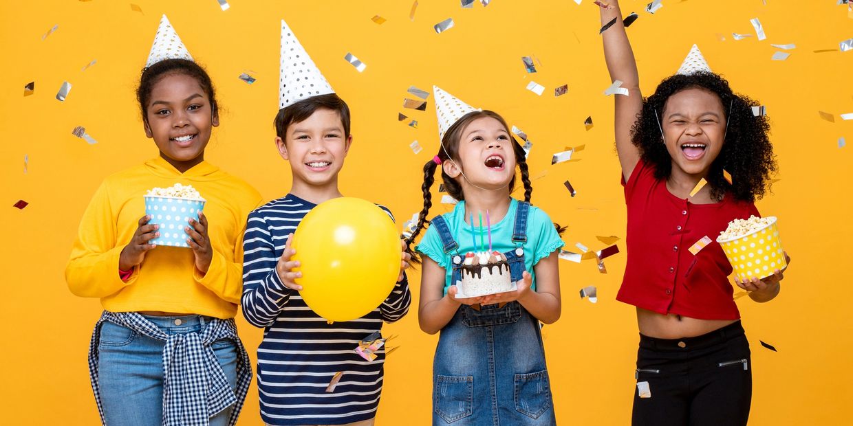 Four kids wearing party hats celebrate with cake, balloons, and popcorn against a yellow background.