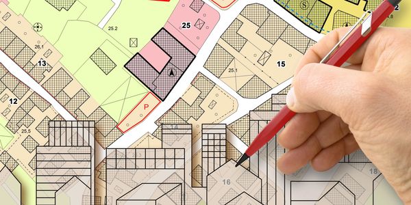 Hand holding a red pen over a detailed urban planning map.