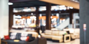 Blurred image of a furniture store interior with sofas and bright lights.