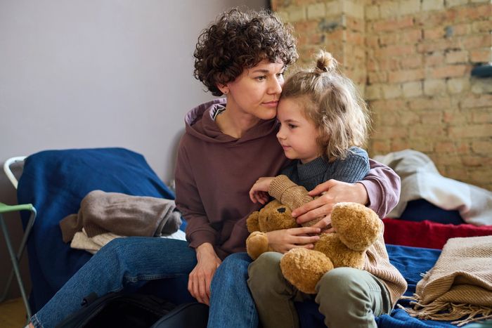 A mother comforting her child holding a teddy bear on a bed.