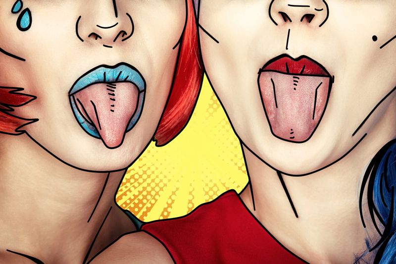 Portrait of young women in comic pop art make-up style. Females in red and blue wigs on yellow - orange cartoon background. Girls show each other tongues