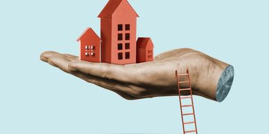 A hand holds miniature house models with a ladder leaning against it.