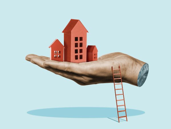 A surreal hand holds miniature red houses with a ladder leaning against the wrist.