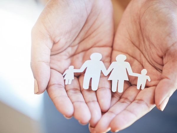 Hands holding paper cutout of a family with two adults and two children.
