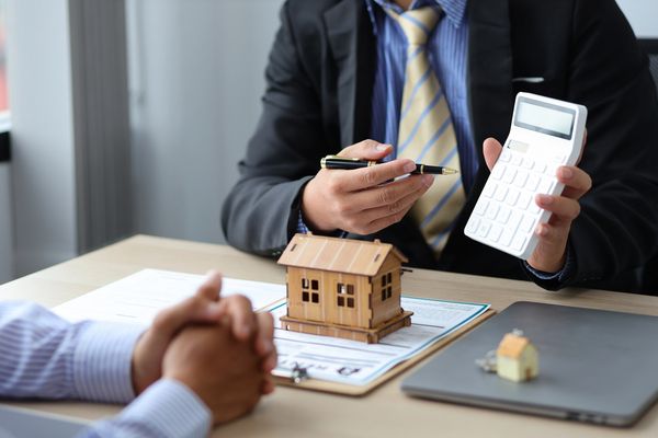  Real estate agent holding a calculator and pen, explaining finance to a client across a desk 
