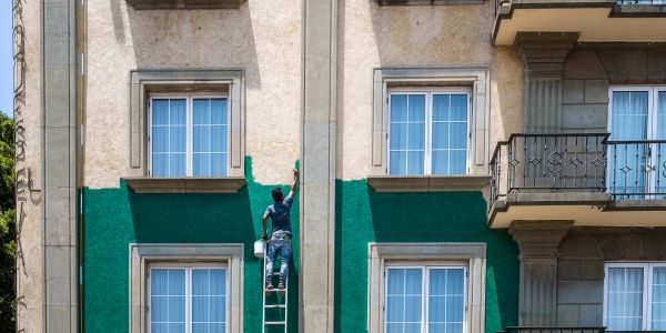 Hombre pintando la fachada verde de un edificio.