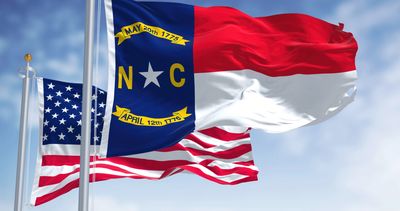 North Carolina and United States flags waving against a clear sky.