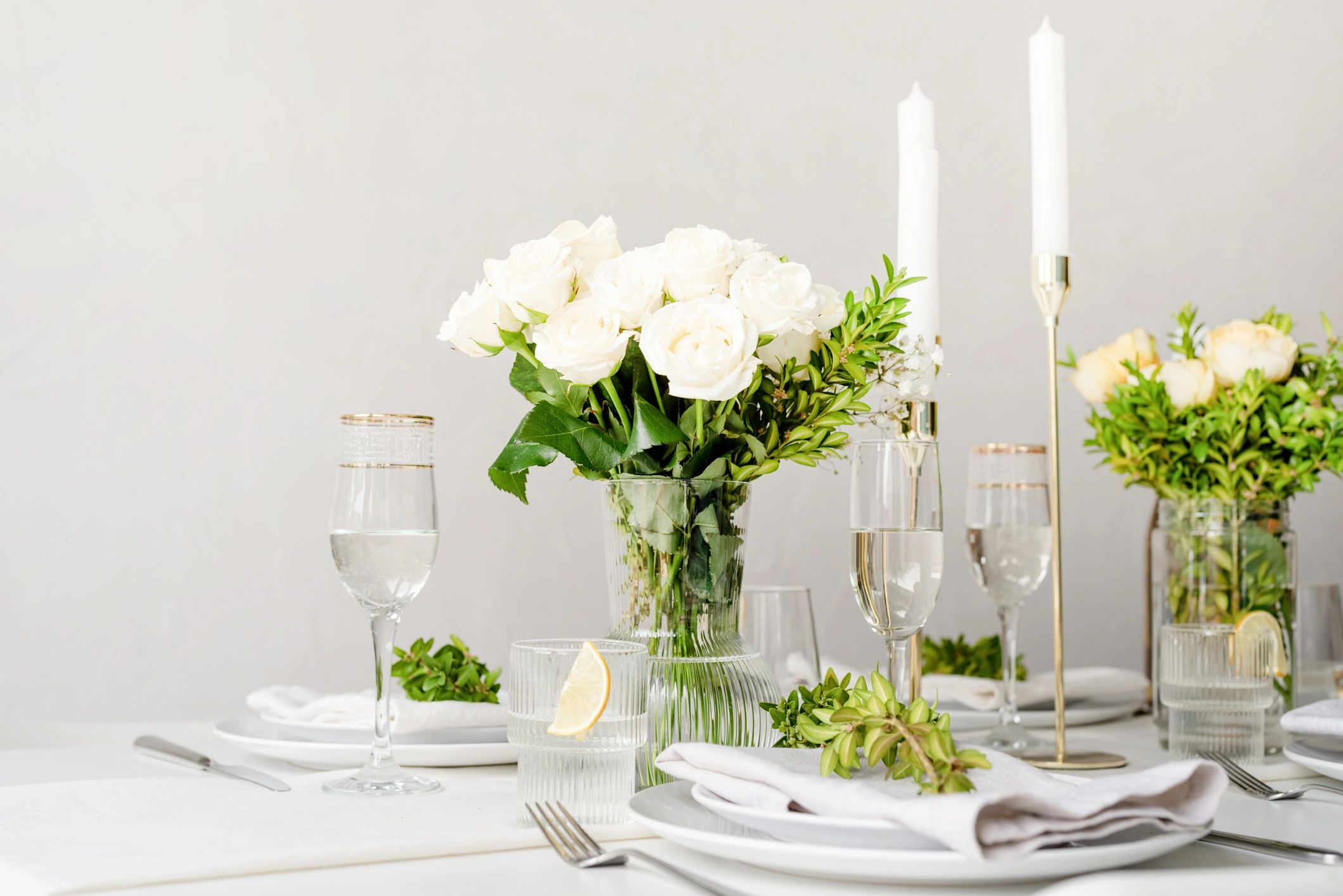 Elegant white floral centerpiece with candles on a refined dining table.
