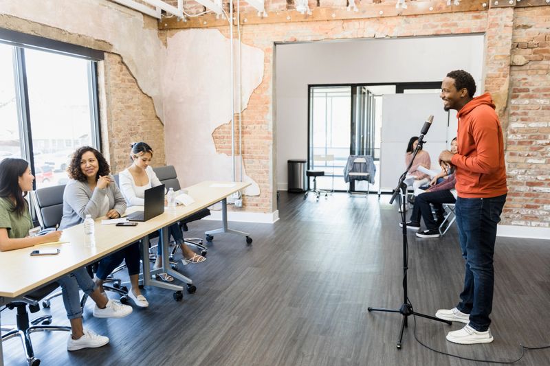 The young adult man smiles as he stands in front of the panel of judges to recite lines.