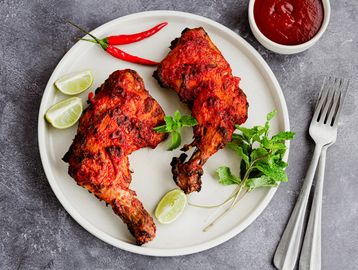 Grilled chicken legs with lime, red chili, and mint on a white plate with ketchup.