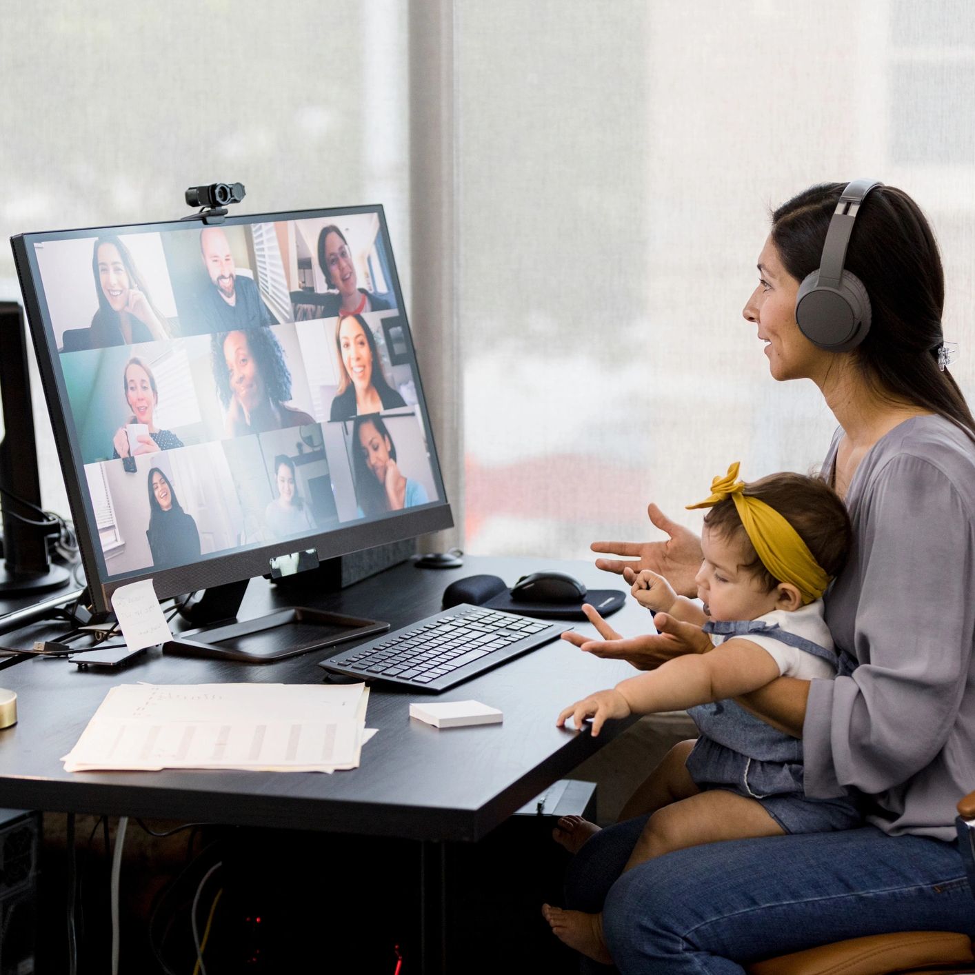 Woman with baby attends a virtual meeting wearing headphones.
