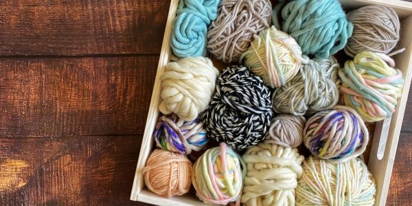 A wooden box filled with colorful yarn balls on a wooden surface.
