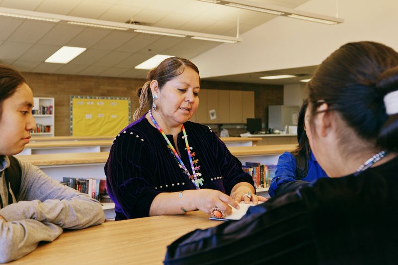 An Indigenous Navajo high school teacher with a group of students in a school library.