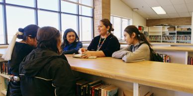A teacher and students discuss at a library table.