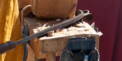 A blacksmith shaping a metal bar on a wooden workbench with a vise.