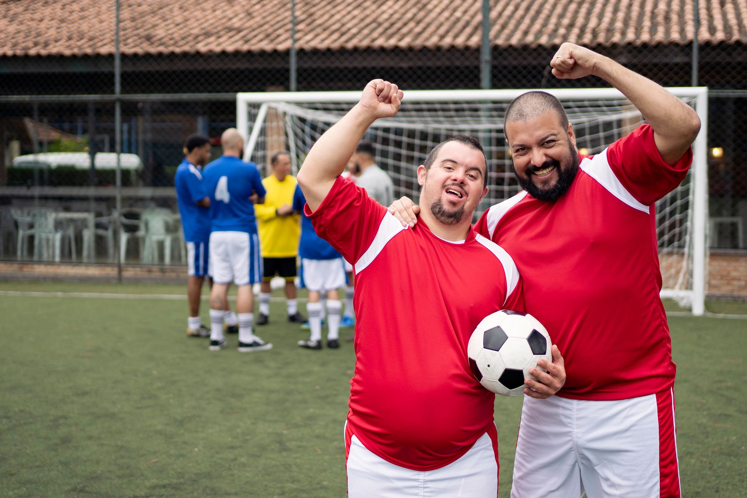 Two joyful soccer players in red celebrate on the field, holding a soccer ball.