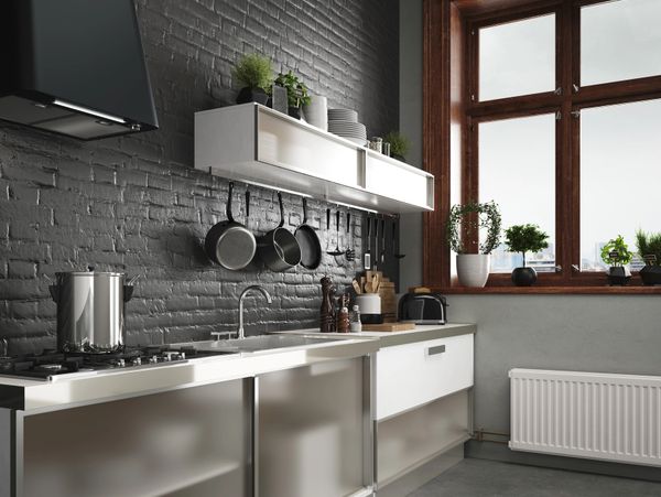 Modern kitchen with gray brick wall, stainless steel cabinets, and large window.