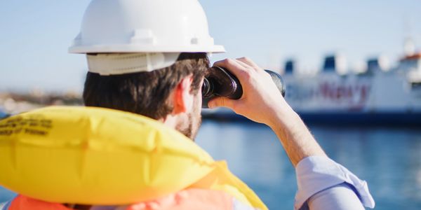 Man in safety gear looking through binoculars near water.