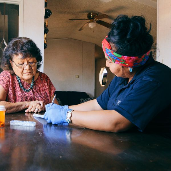 A healthcare worker consults an elderly woman about her medication at a table.