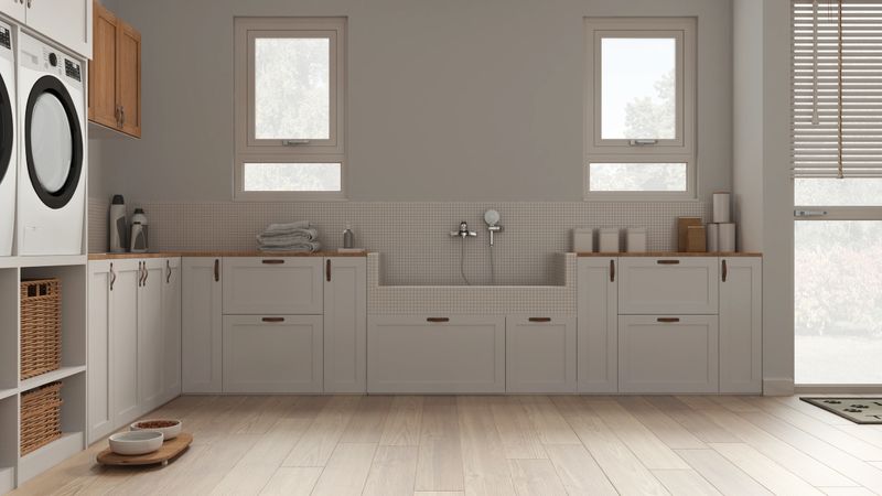 Pet friendly laundry room, space devoted to pets, mudroom in white tones. Parquet, cabinets and windows, dog bath shower with tiles, accessories and faucet. Cozy interior design idea