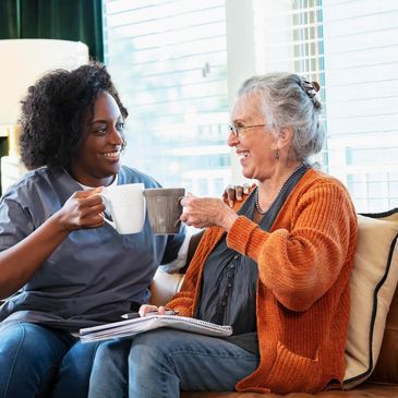 A caregiver and elderly woman sharing a joyful moment with coffee.
