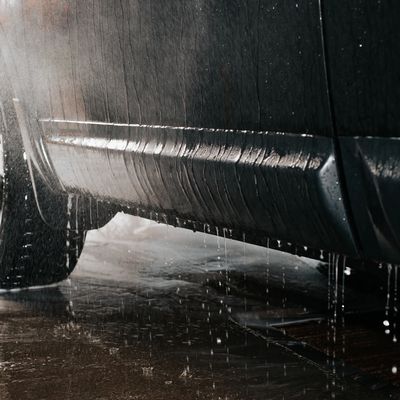 Close-up of a car being washed with water spraying over the wheel and side panel.