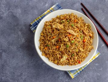 A bowl of chicken fried rice with chopsticks on a cloth napkin.