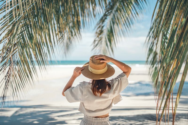 Summer beach vacation concept, Happy woman with hat relaxing at the seaside and looking away, in the summer against a backdrop of palm trees and sea beach.