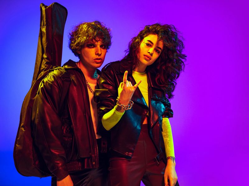 Music. Young couple of rock-and-roll musicians wearing black leather outfits gesturing, shouting and posing on blue yellow background in neon light. Concept of style, art, fashion and youth