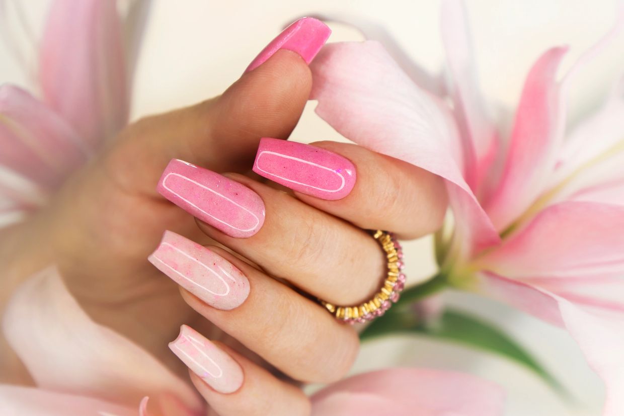 Hand with pink ombre nails holding a pink flower.