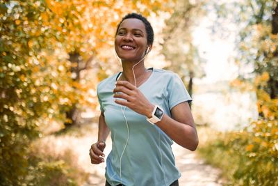 Woman jogging outdoors in autumn with earphones and smartwatch.