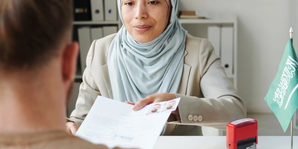 A woman in a hijab interviews a man with documents.