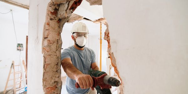Construction worker demolishing a wall with a power drill.